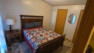 A bedroom with a wooden bed, a nightstand with a lamp, a door, and a mirror on the wall.