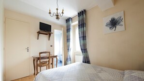 Un dormitorio con cama, escritorio, silla, televisor en la pared y ventana con cortinas.