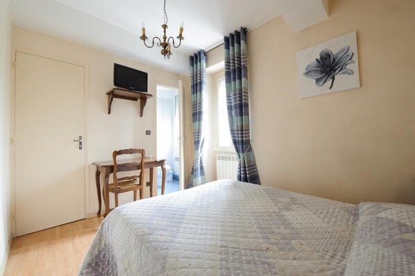 A bedroom with a bed, a desk, a chair, a television on the wall, and a window with curtains. - L'Esplanade (Sens)