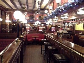 A bar area with a wooden counter, bar stools, and a red booth. - L'Esplanade (Sens)