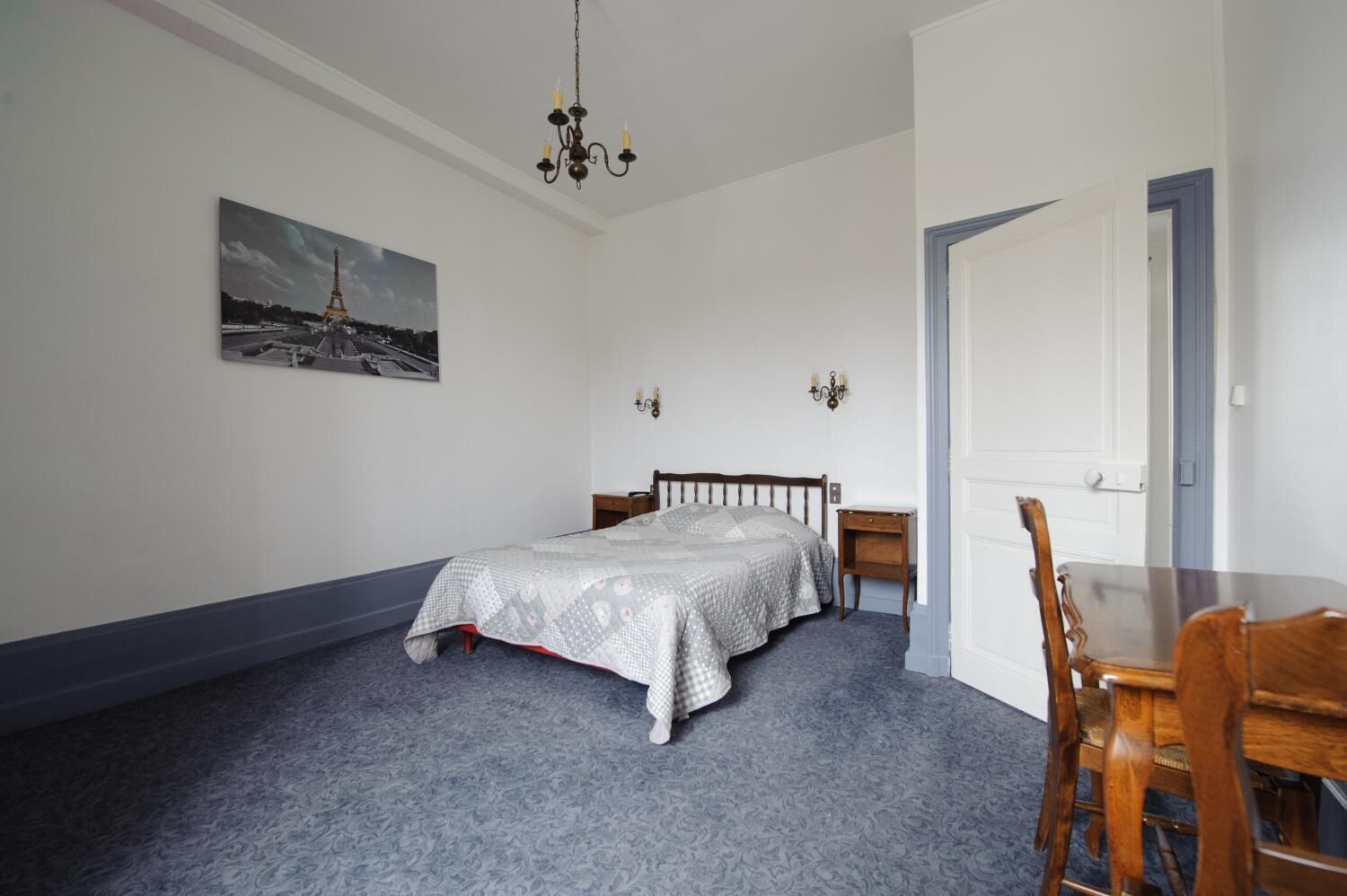 Une chambre à coucher avec un lit, une chaise, une table, un lustre, un tableau et une porte.