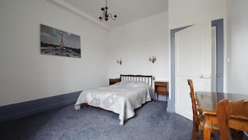 Une chambre à coucher avec un lit, une chaise, une table, un lustre, un tableau et une porte.