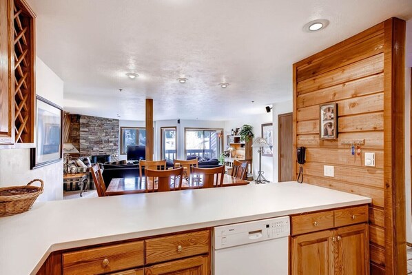 A spacious kitchen with wooden cabinetry, a central island, and a stone fireplace. - Cimarron - great condo! Slopes and town within easy walking distance  (Breckenridge)