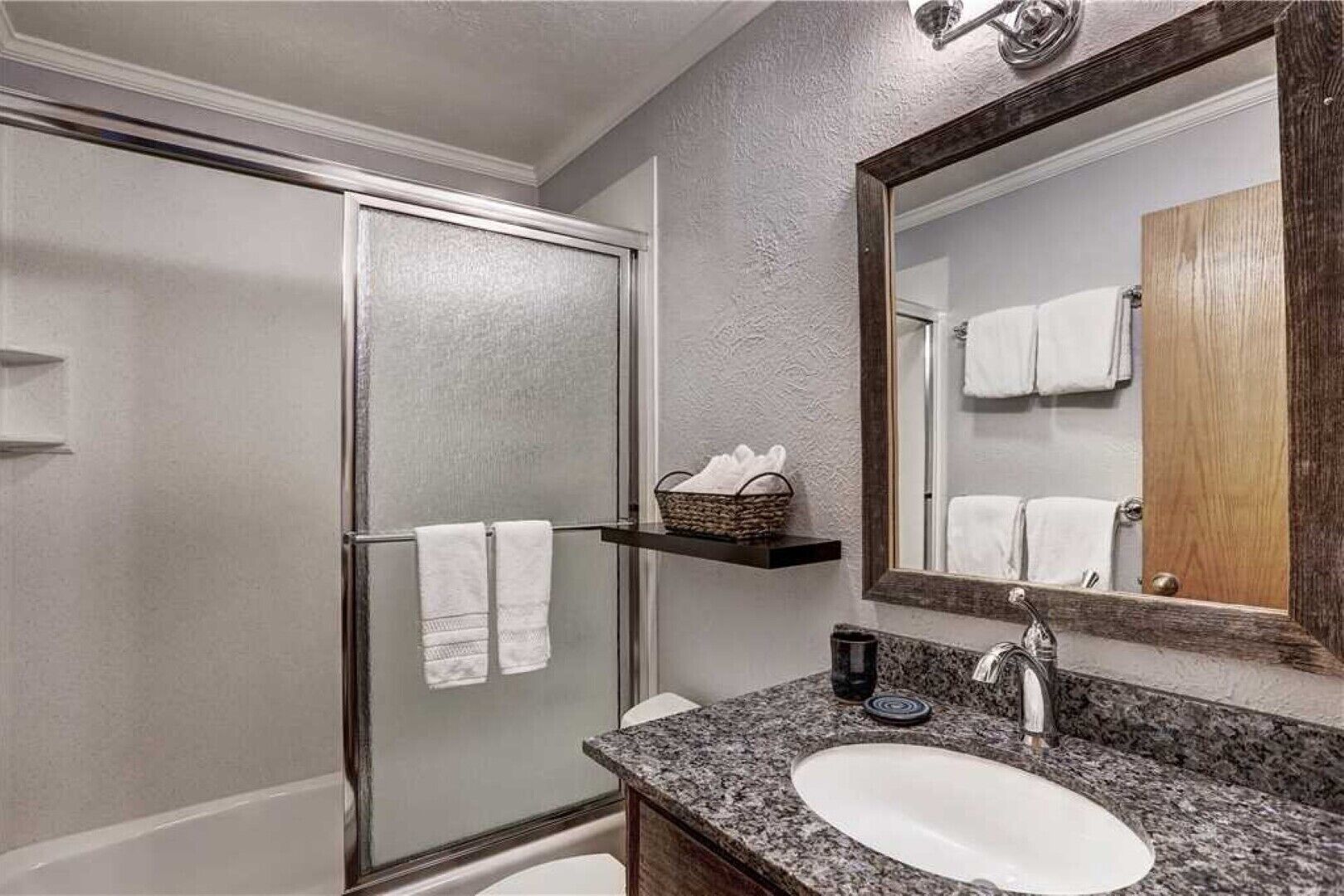 Een badkamer met een douche, wastafel, spiegel en handdoekhouder.