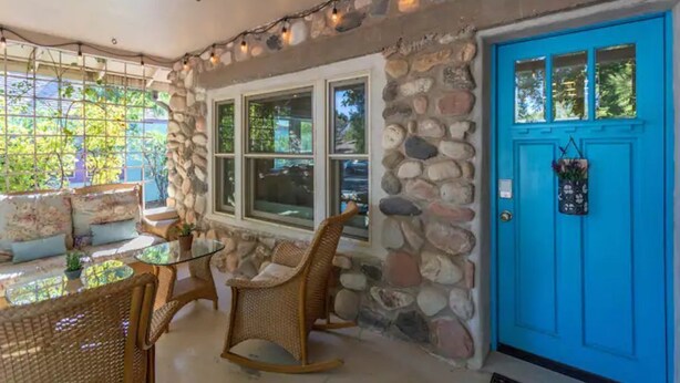 A stone wall exterior with a blue door, wicker furniture, and a glass table.