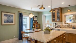 A kitchen with a large island, wooden cabinets, pendant lighting, and a dining area with chairs and a table.