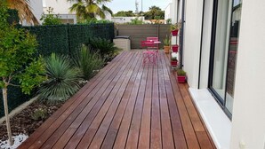 A wooden deck with a green hedge, a small tree, and a potted plant. - Chambre Cosy (Agde)