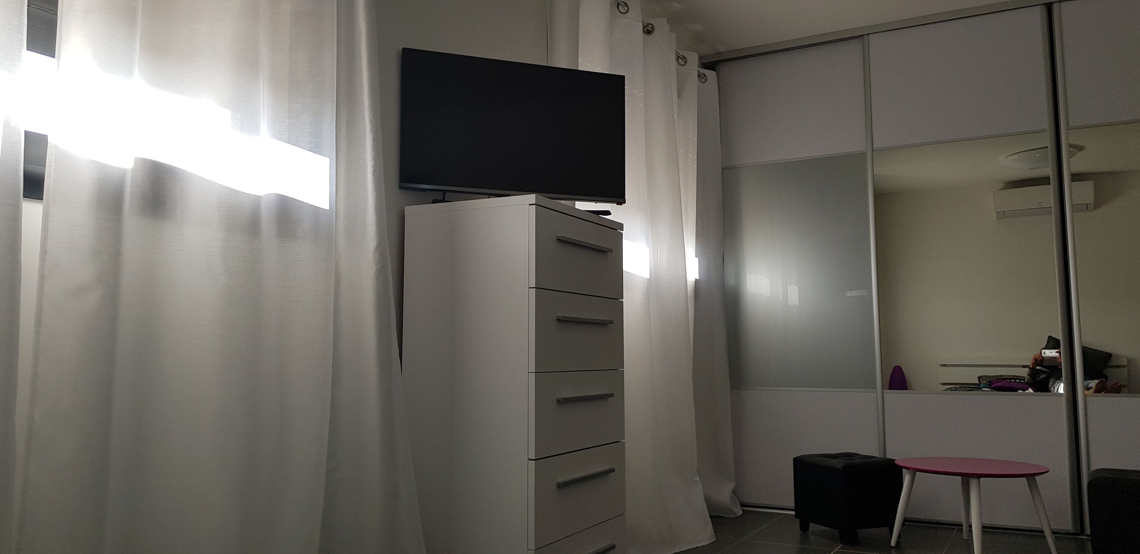 Habitació amb televisió de pantalla plana penjada en un moble, porta d'armari corredissa, taula petita i una cadira.