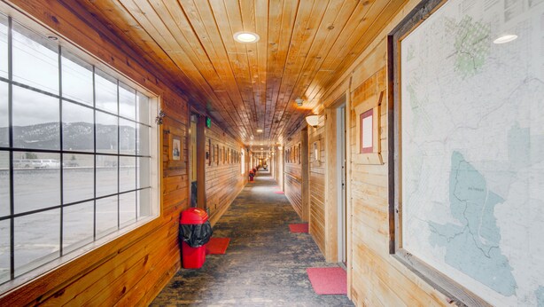 A long hallway with wooden walls and a carpeted floor, leading to a large window with a view of a snowy landscape. - Livingston Inn - Historic (Livingston)