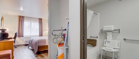 A hotel room with a bed, a desk, a chair, a bathroom with a shower, and a toilet.