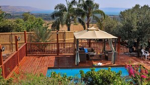 A wooden deck with a pool, a covered seating area, and a view of the landscape. - The Golan Cabin (Had Nes)
