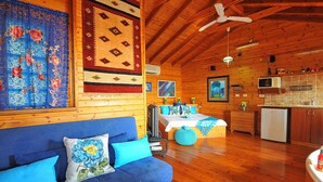 A cozy cabin interior with a blue sofa, wooden walls, a ceiling fan, a kitchen area, and a dining table with a blue tablecloth. - The Golan Cabin (Had Nes)