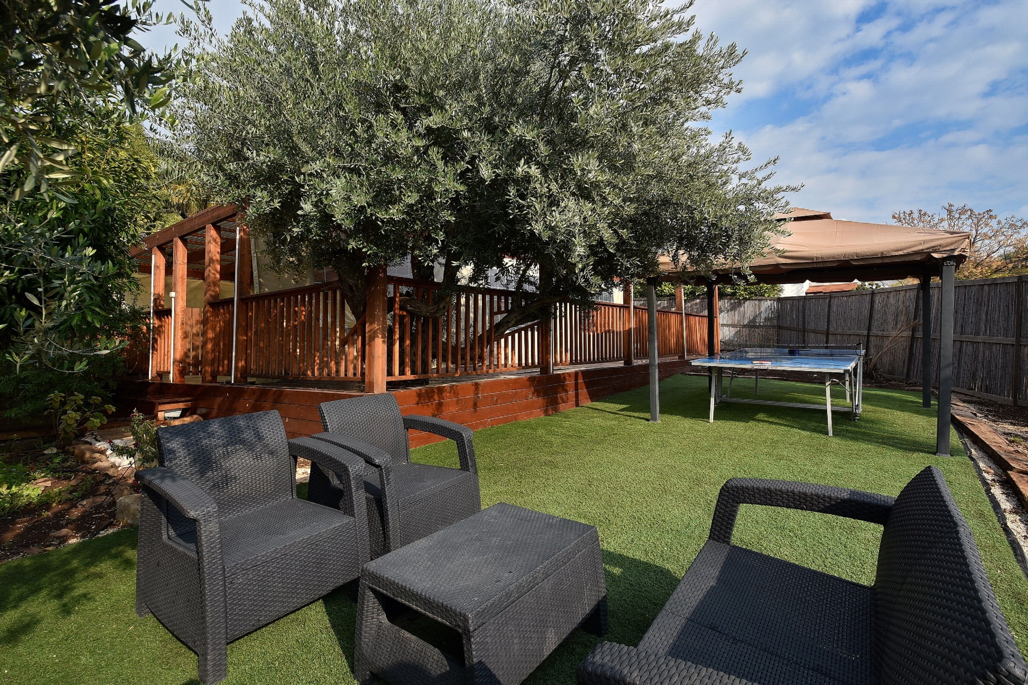Un jardin avec une pelouse artificielle, une terrasse en bois, un trampoline et des meubles en osier.