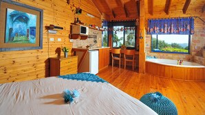 A wooden cabin with a bed, a kitchenette, a dining area, and a bathroom with a window view. - The Golan Cabin (Had Nes)