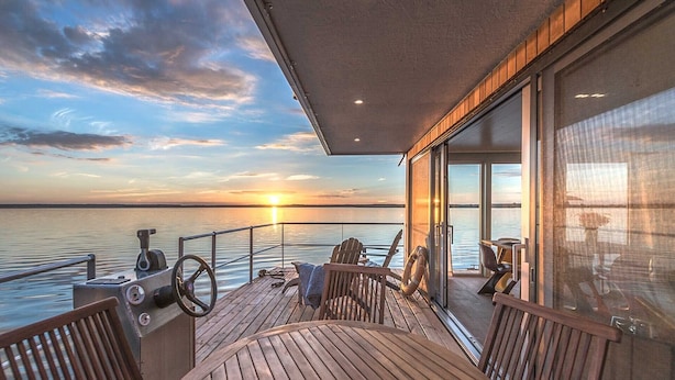 Een houten terras met een tafel en stoelen, uitkijkend over een wateroppervlak bij zonsondergang.