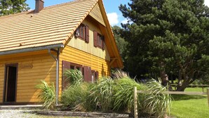 Ein gelbes Holzhaus mit Ziegeldach, Schornstein und einem Schild mit der Aufschrift 'GITE AU ROCHER 16A'.