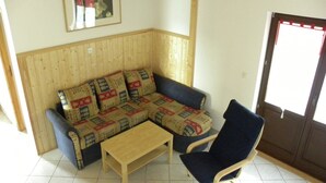 Ein Eckwohnzimmer mit einer Wandpaneele aus Holz, einem blauen Sofa mit gemusterten Kissen, einem Holztisch und einem blauen Schaukelstuhl.
