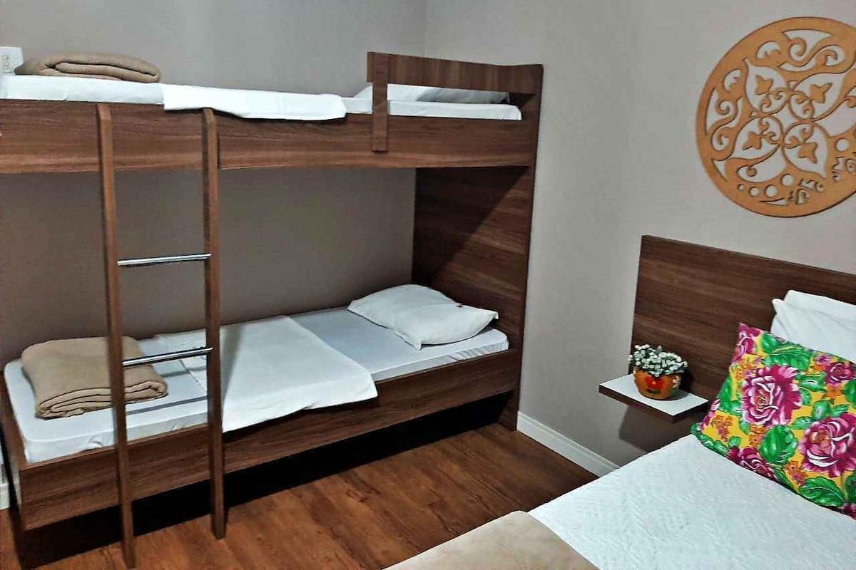 Una cama individual superpuesta con escalera, una mesita de noche con una planta y un cojín de colores.