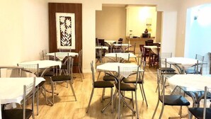 Zona pranzo con diversi tavoli e sedie, angolo cottura sullo sfondo e un'ampia opera d'arte incorniciata al muro.