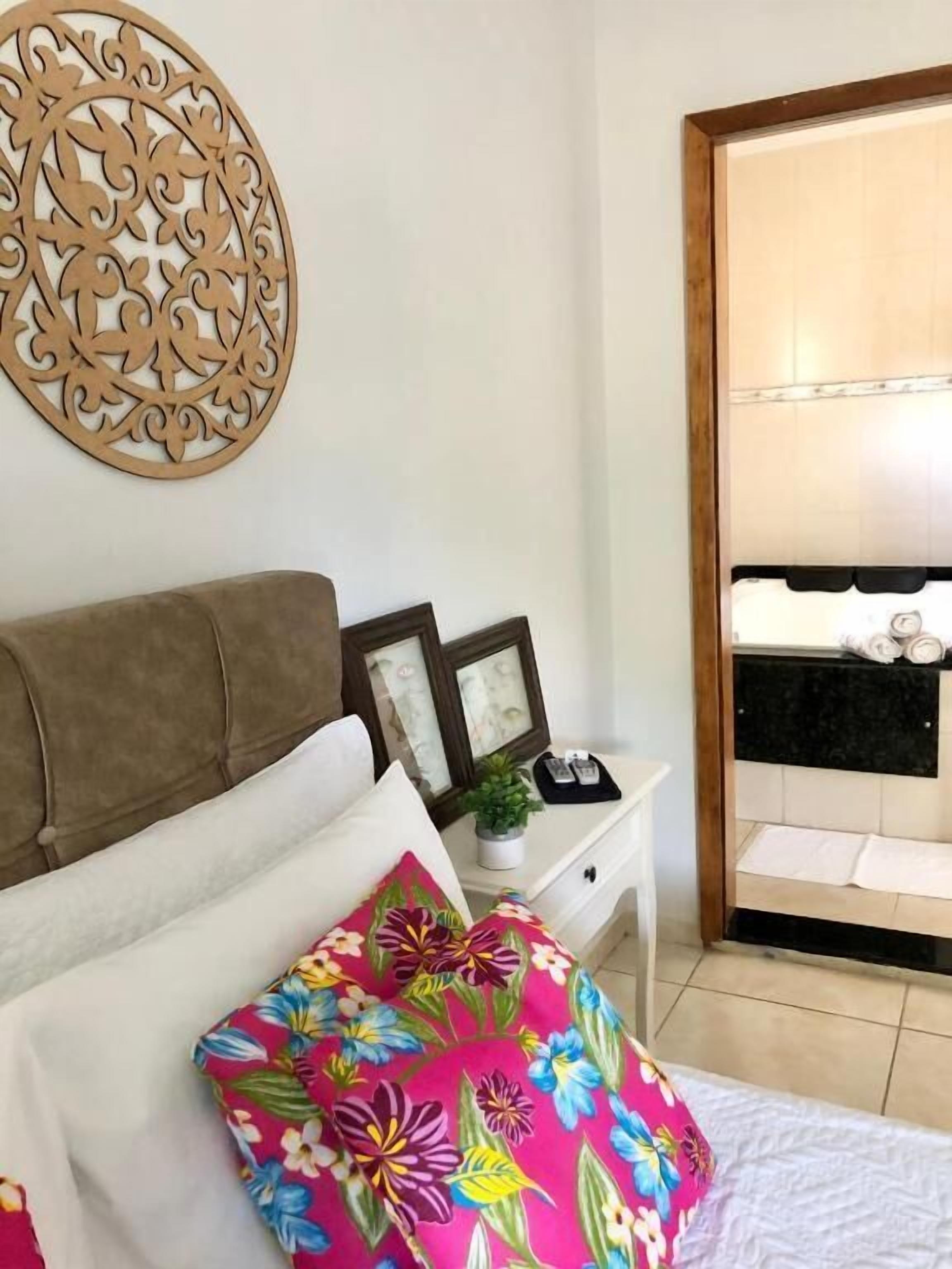 A bedroom with a bed, a nightstand, a decorative wall piece, and a view of a balcony with a towel rack.