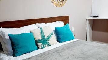 Una cama con una manta gris, almohadas blancas y dos almohadas color turquesa. Encima de la cama hay dos elementos decorativos en la pared.