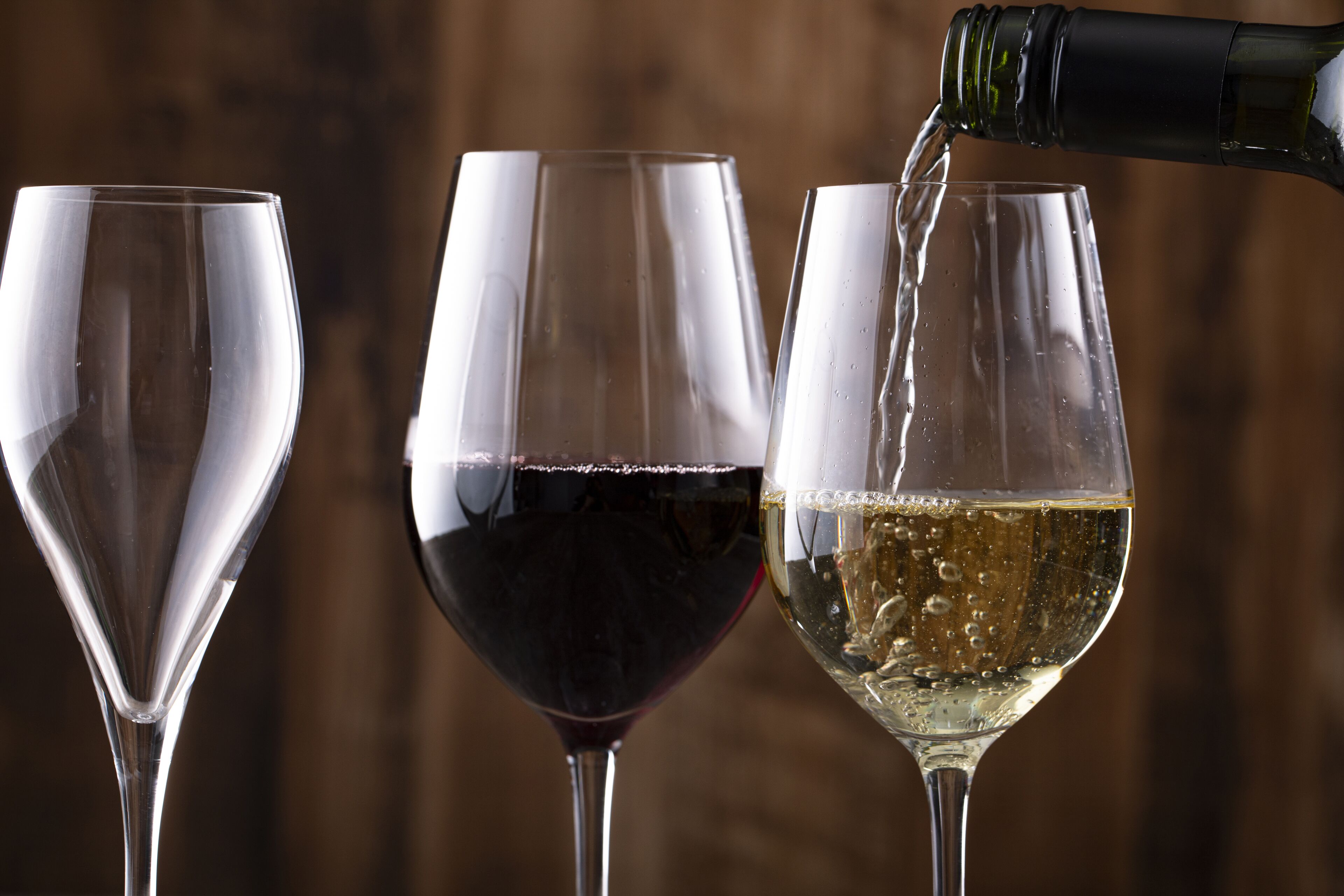 Three wine glasses, one with red wine and another with white wine, being filled from a bottle.