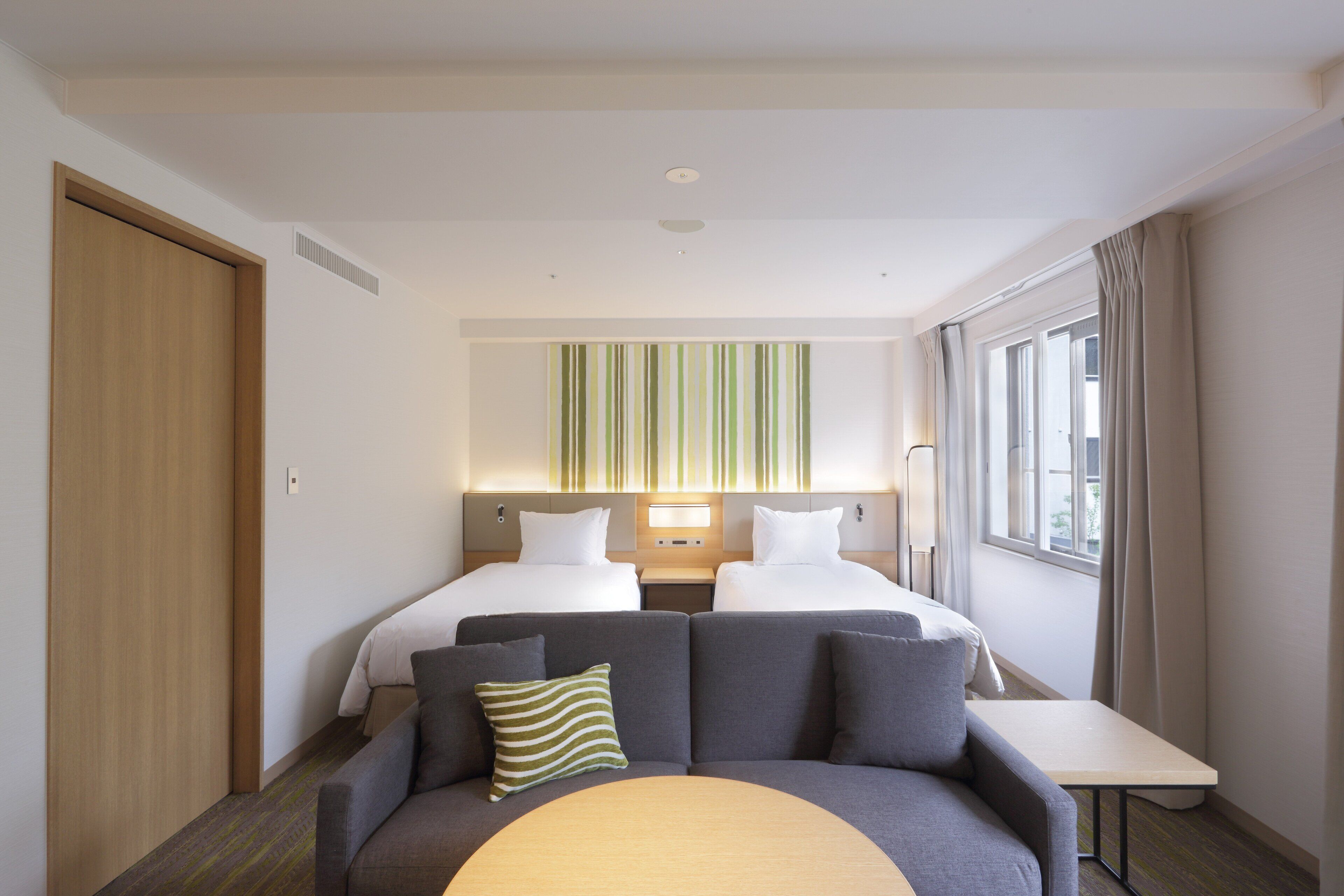Een hotelkamer met twee bedden, een bank, een tafeltje en een raam met gordijnen.