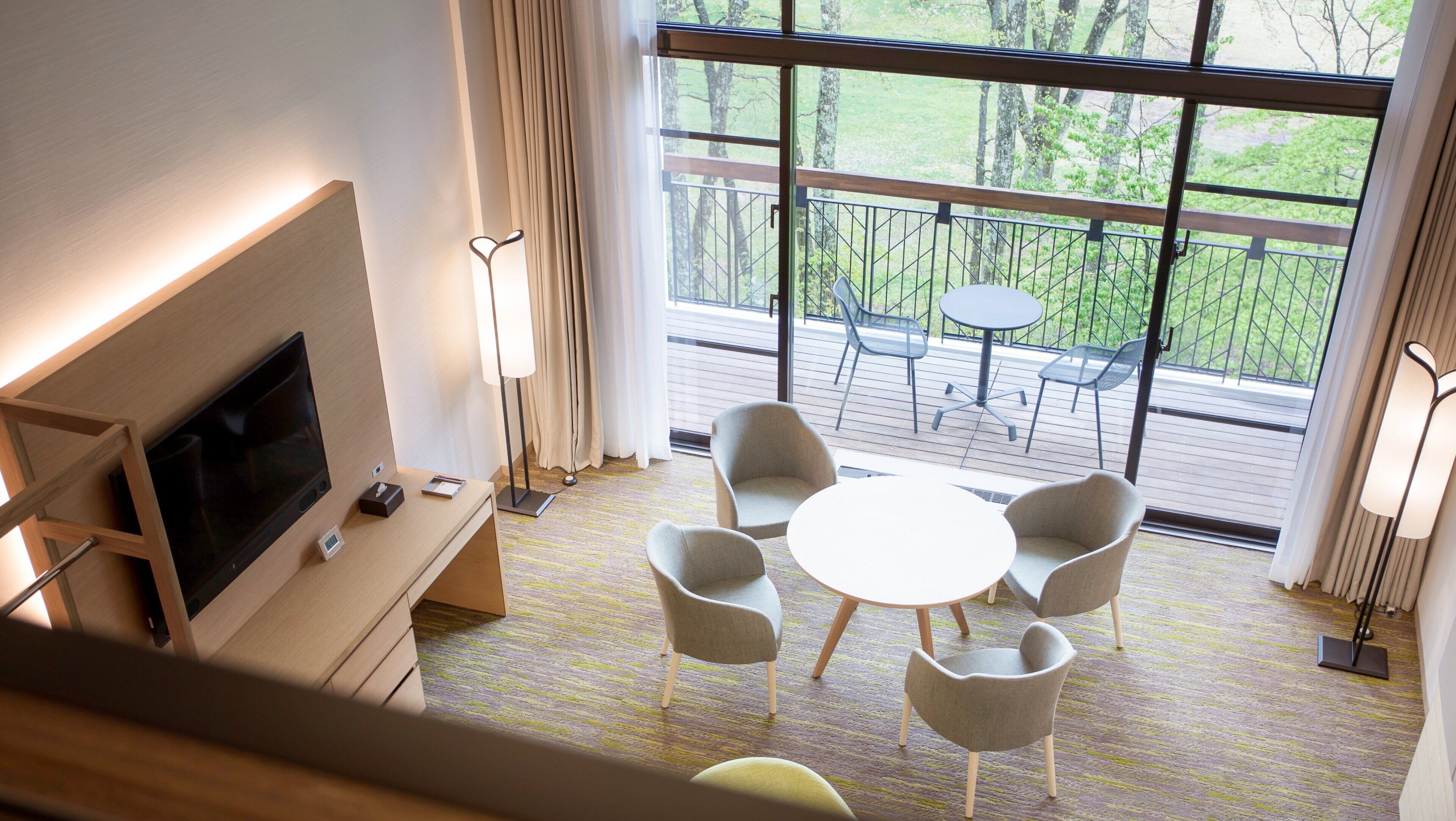 Une chambre d’hôtel moderne équipée d’une télévision, d’une table de chevet et d’une grande fenêtre donnant sur l’extérieur.