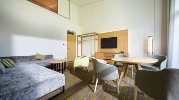 A modern hotel room with a sofa, chairs, a table, and a TV.