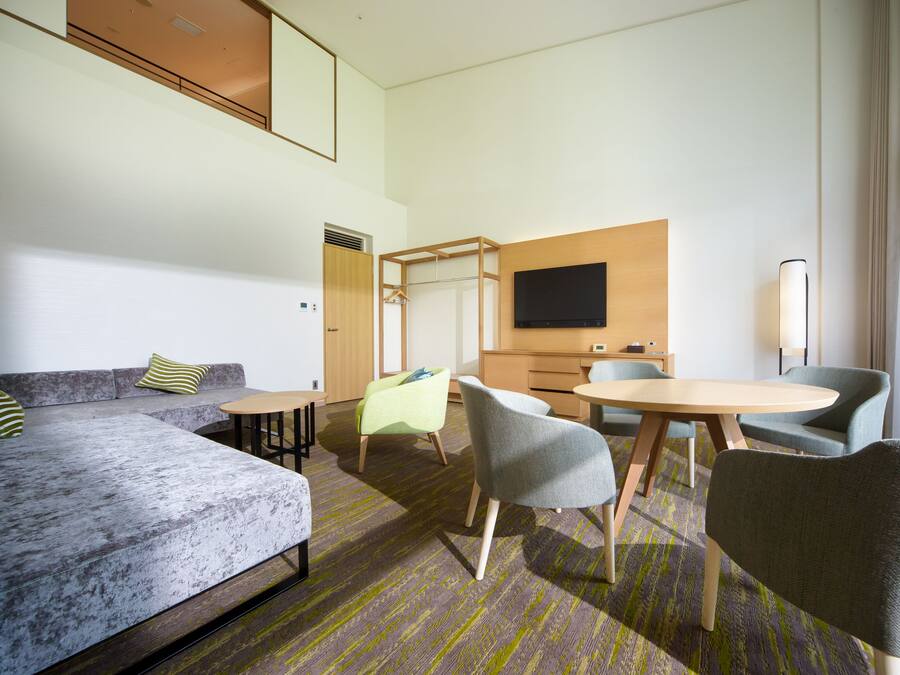 A modern hotel room with a sofa, chairs, a table, and a TV.