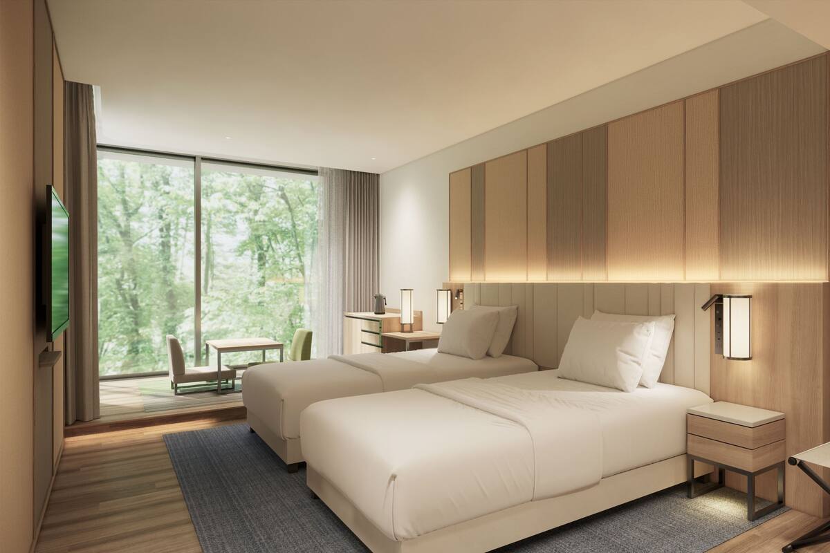 A modern hotel room with two beds, a desk, a chair, and a large window with a view of trees.