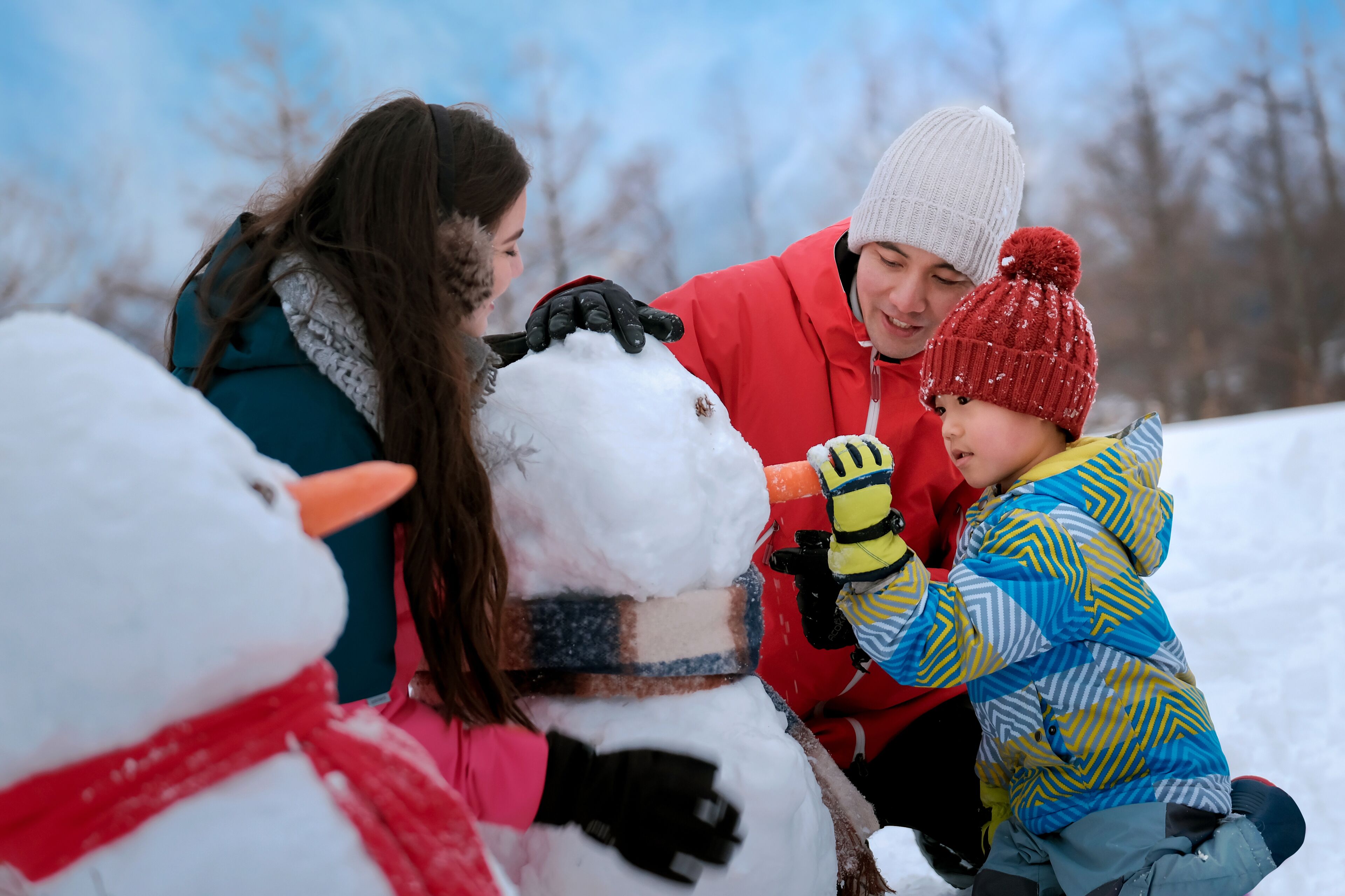 A group of people building a snowman in a snowy outdoor setting.