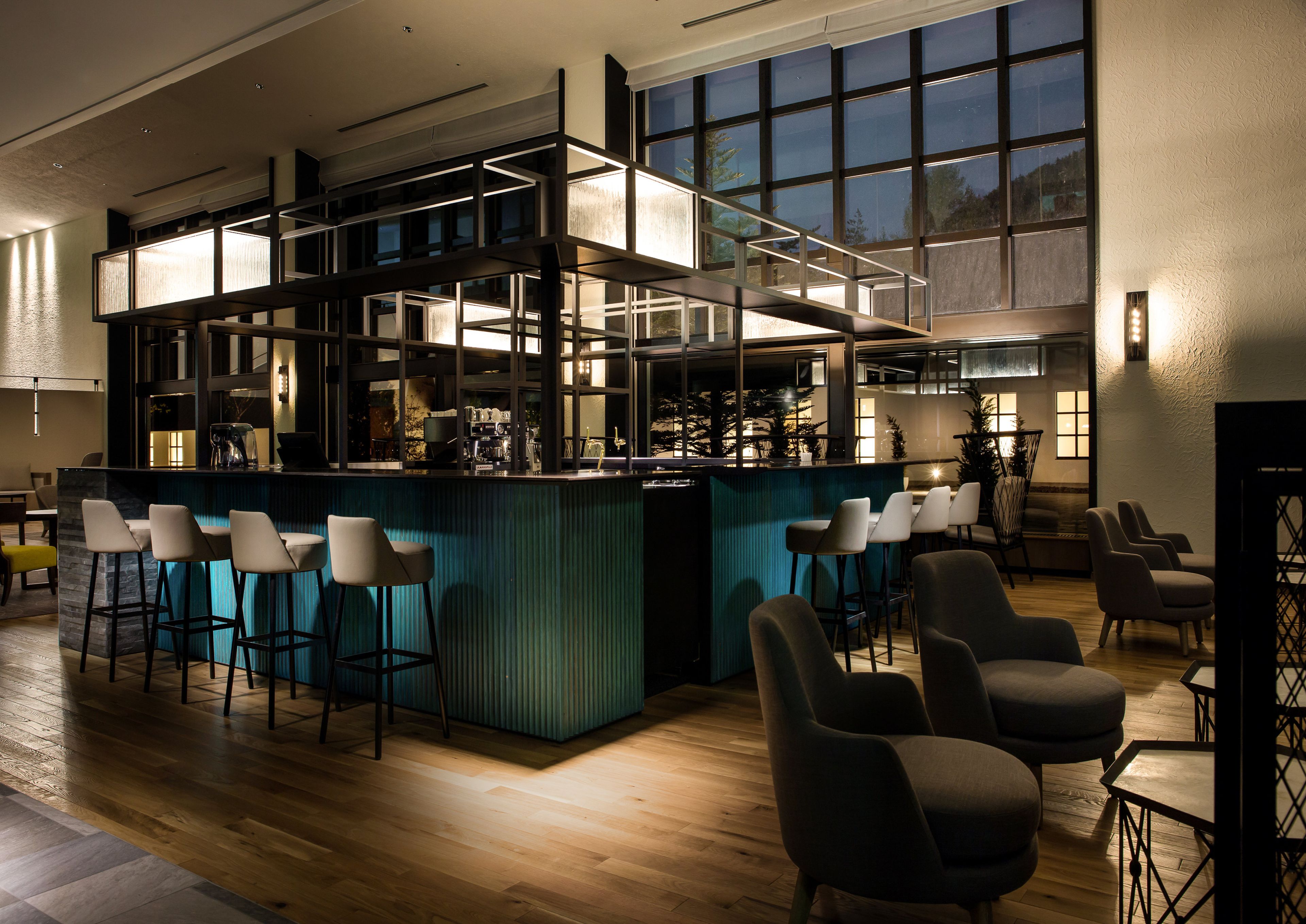 A bar area with a high ceiling, multiple seating options, and a view through large windows.