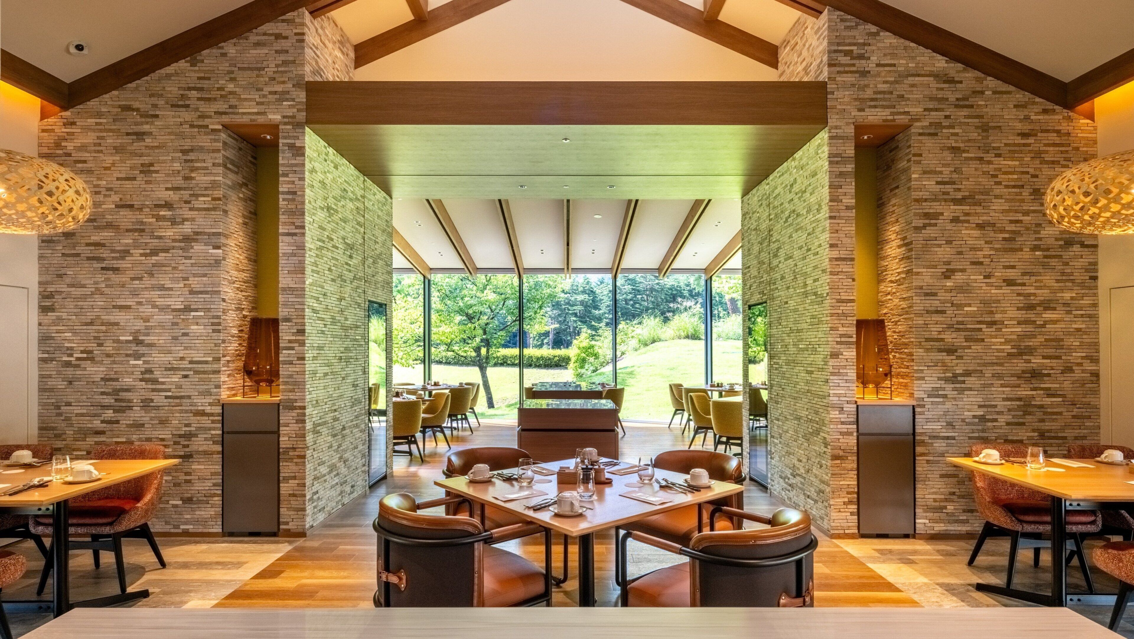 A modern dining area with a large table, multiple chairs, and a view of a garden through large windows.