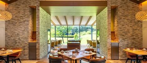 Un comedor moderno con una mesa grande, varias sillas y vistas a un jardín a través de amplios ventanales.
