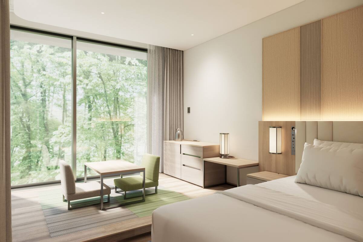A modern hotel room with a large window, a desk, a chair, a bed, and a nightstand with a lamp.