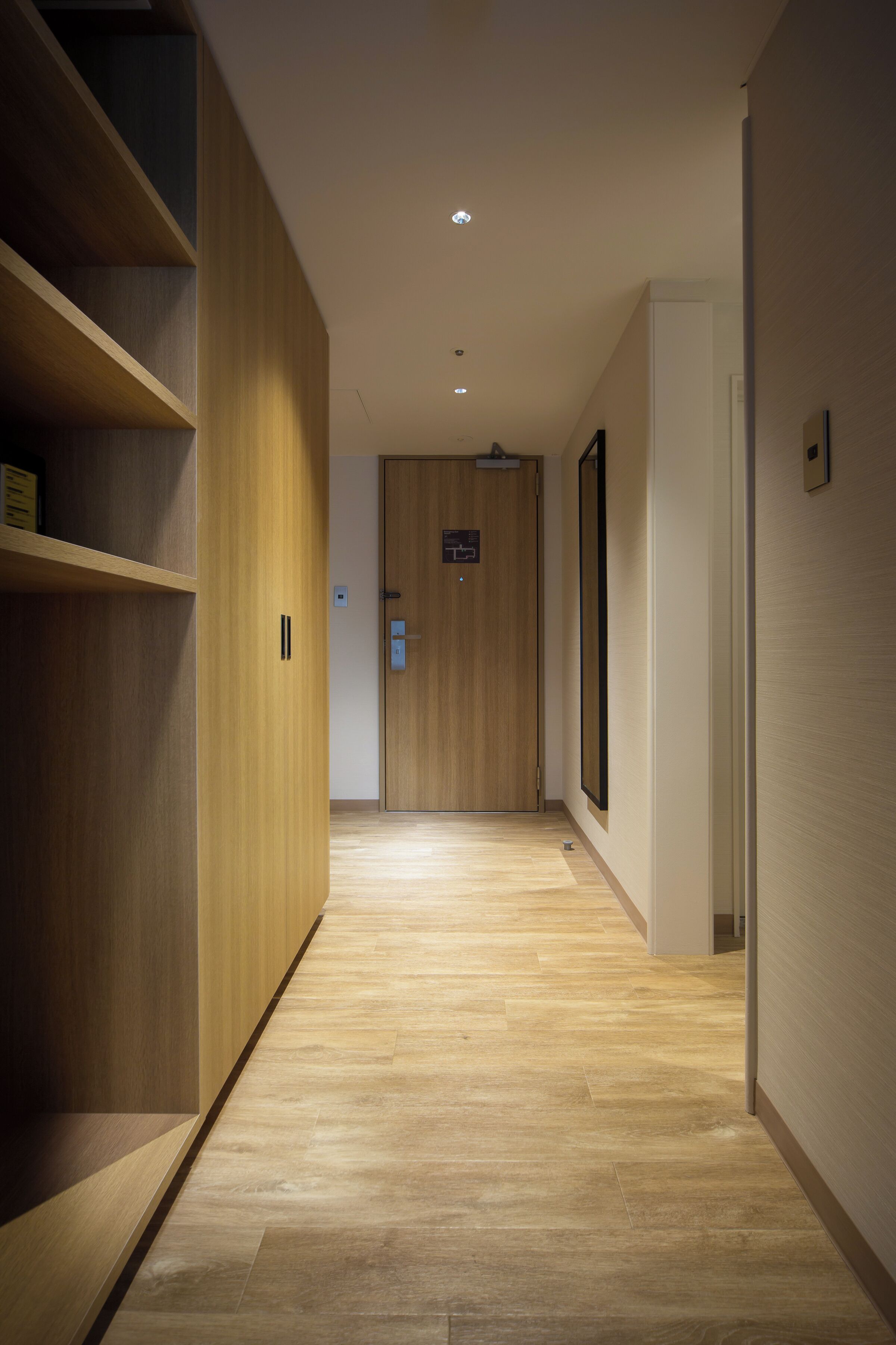 A hallway with wooden flooring and walls, a door at the end, and a light fixture on the ceiling.