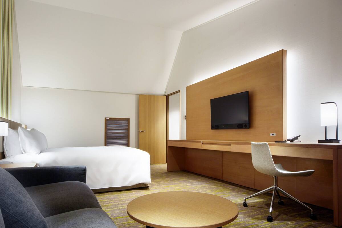 A hotel room with a bed, a desk, a chair, a TV, and a lamp.