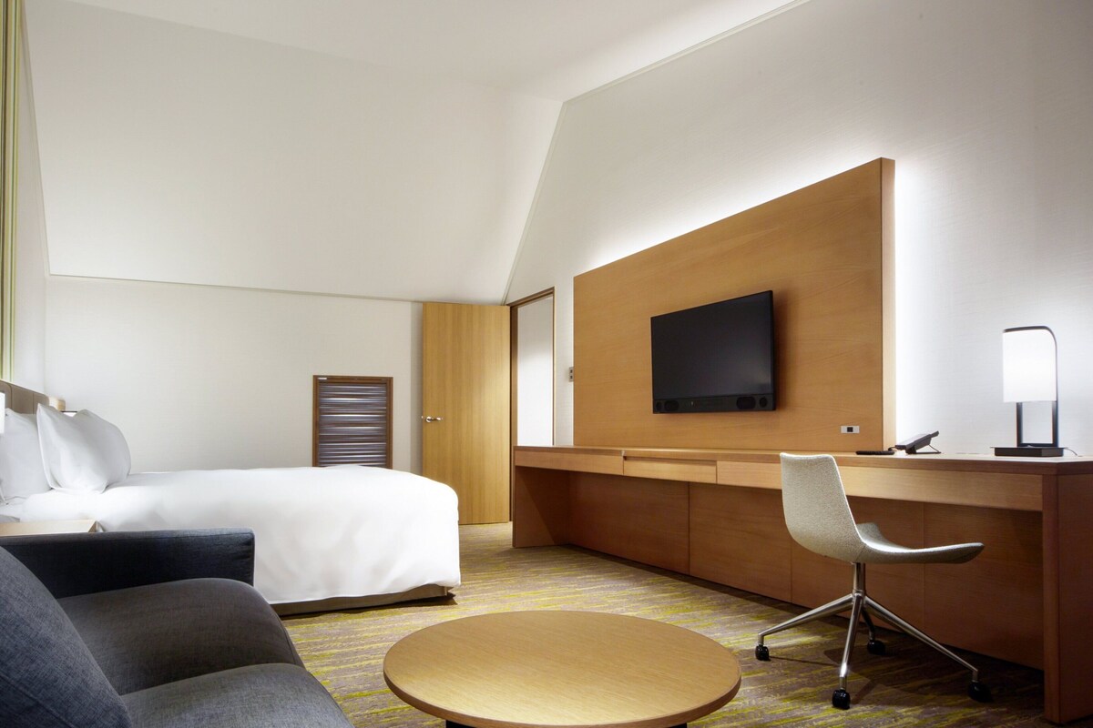 A hotel room with a bed, a desk, a chair, a TV, and a lamp.