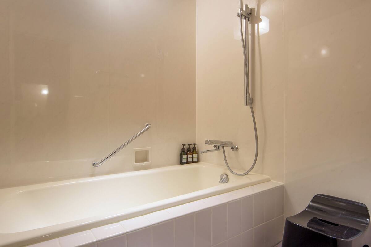 A modern bathroom with a large bathtub, a handheld showerhead, and a small stool.