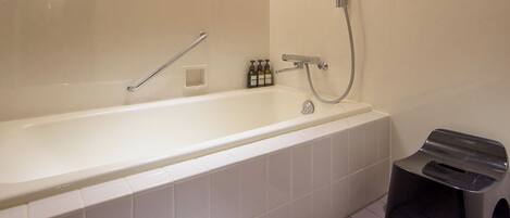 Un baño moderno con una bañera grande, un cabezal de ducha manual y un taburete pequeño.
