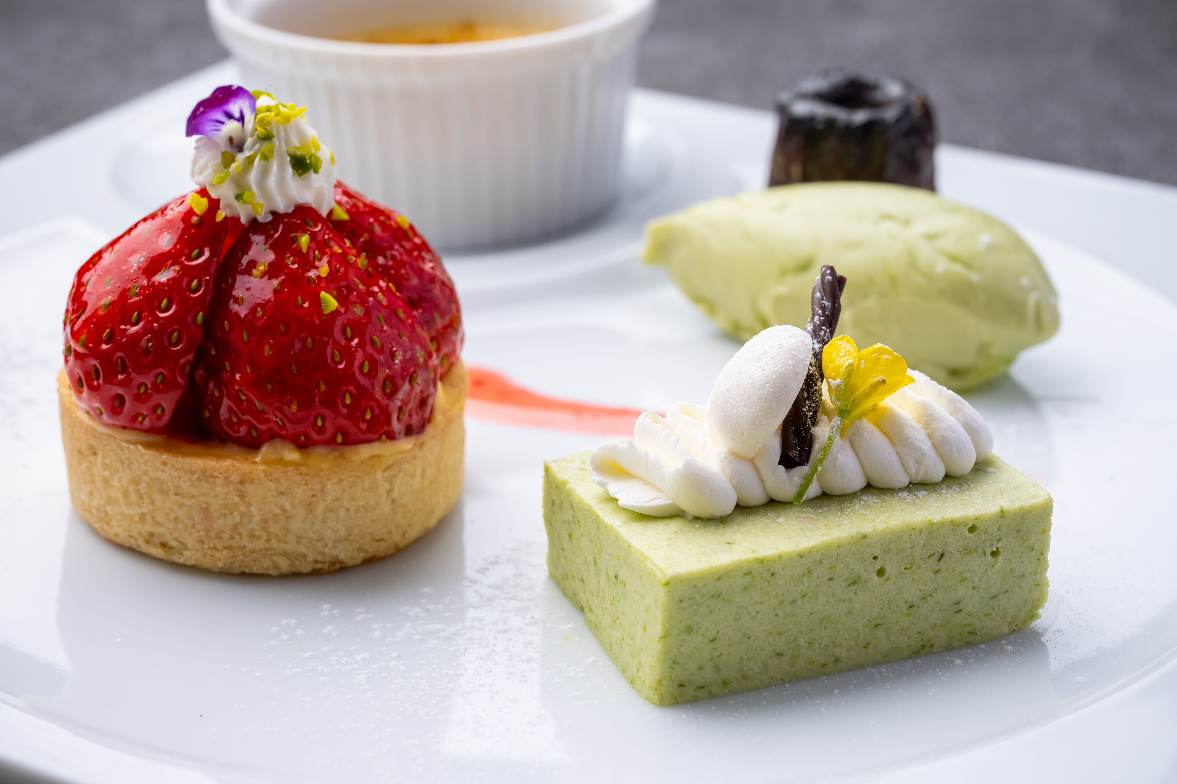 A dessert plate with a strawberry tart, a green mousse, and a chocolate dessert.