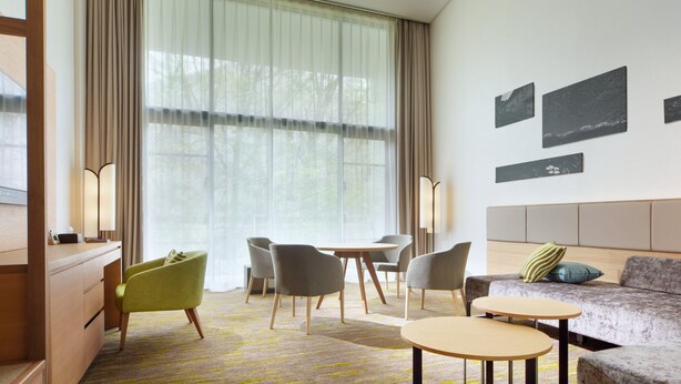 A modern hotel room with a sofa, two armchairs, a small table, a desk, and a large window with sheer curtains. - Holiday Inn Resort Kuroyon by IHG (Omachi)