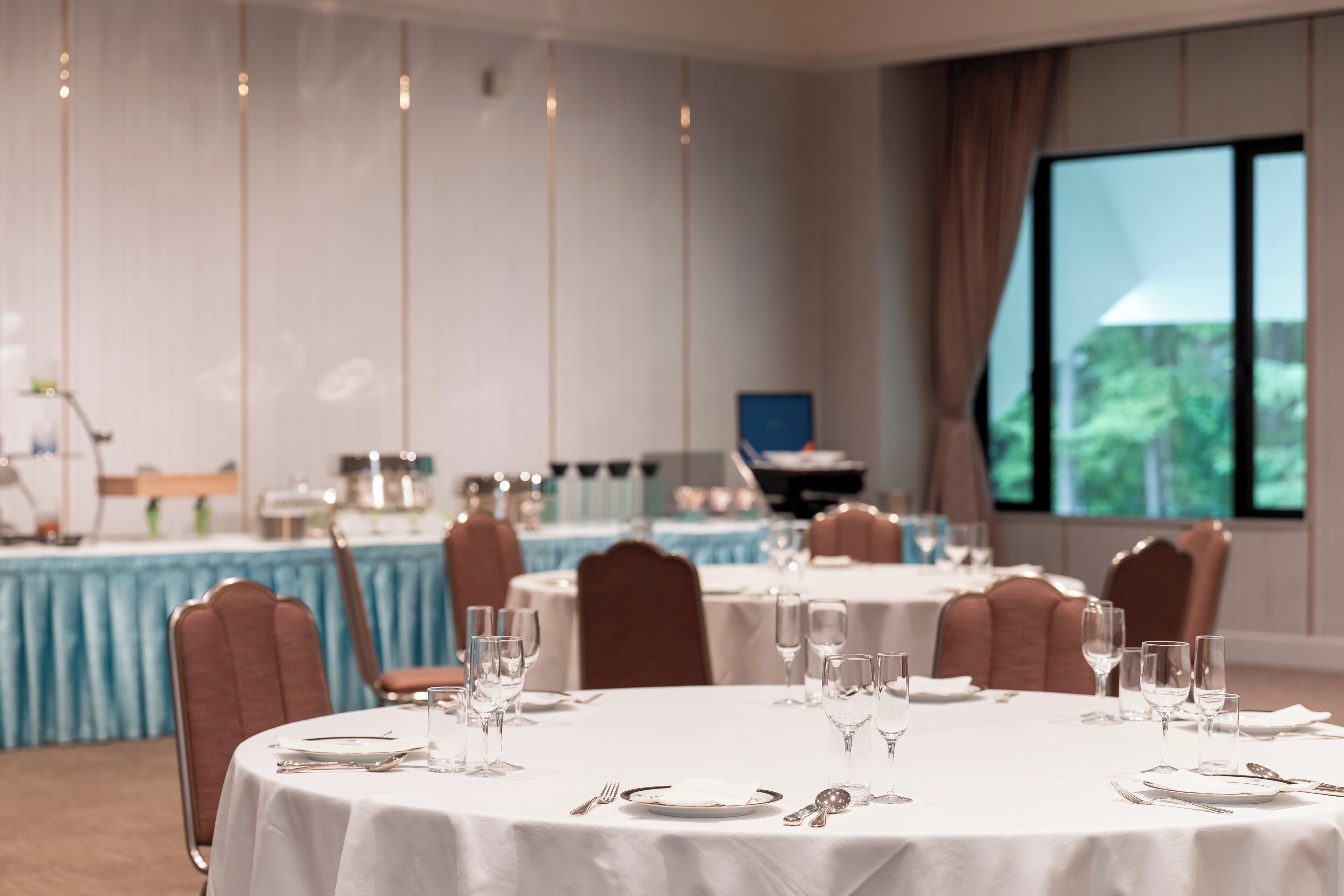 A dining area with round tables set for a meal, chairs, and a bar area in the background.
