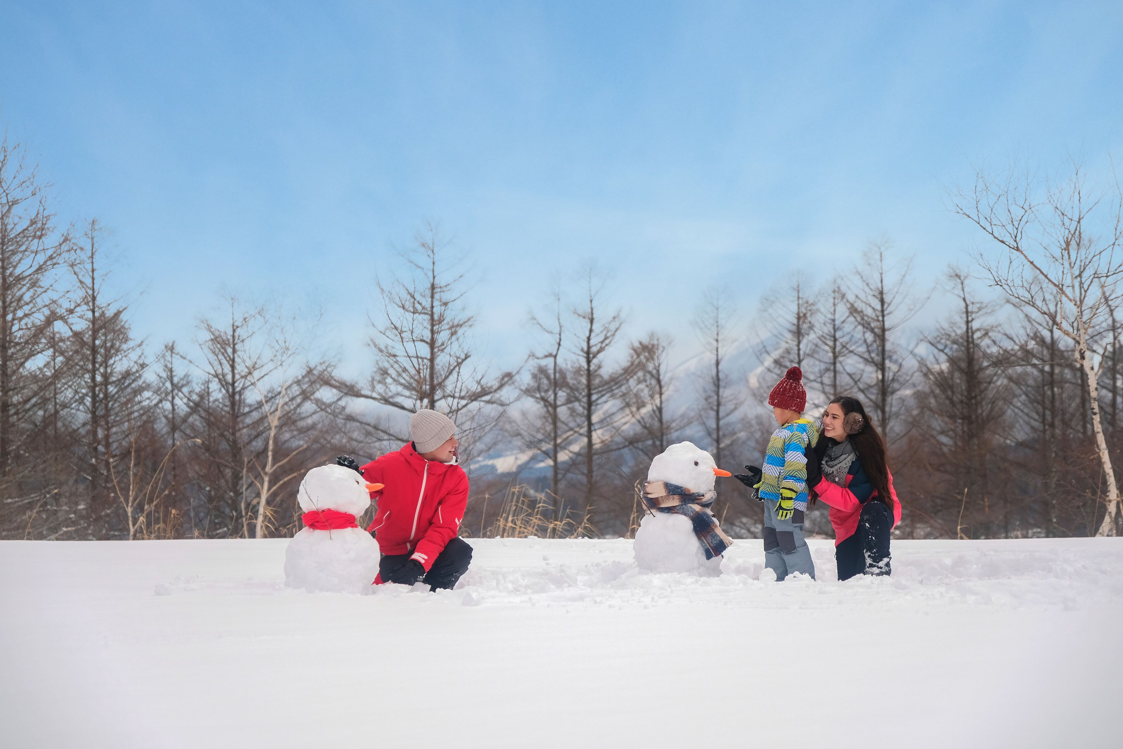 Un grupo de personas construyendo muñecos de nieve en un paisaje nevado.