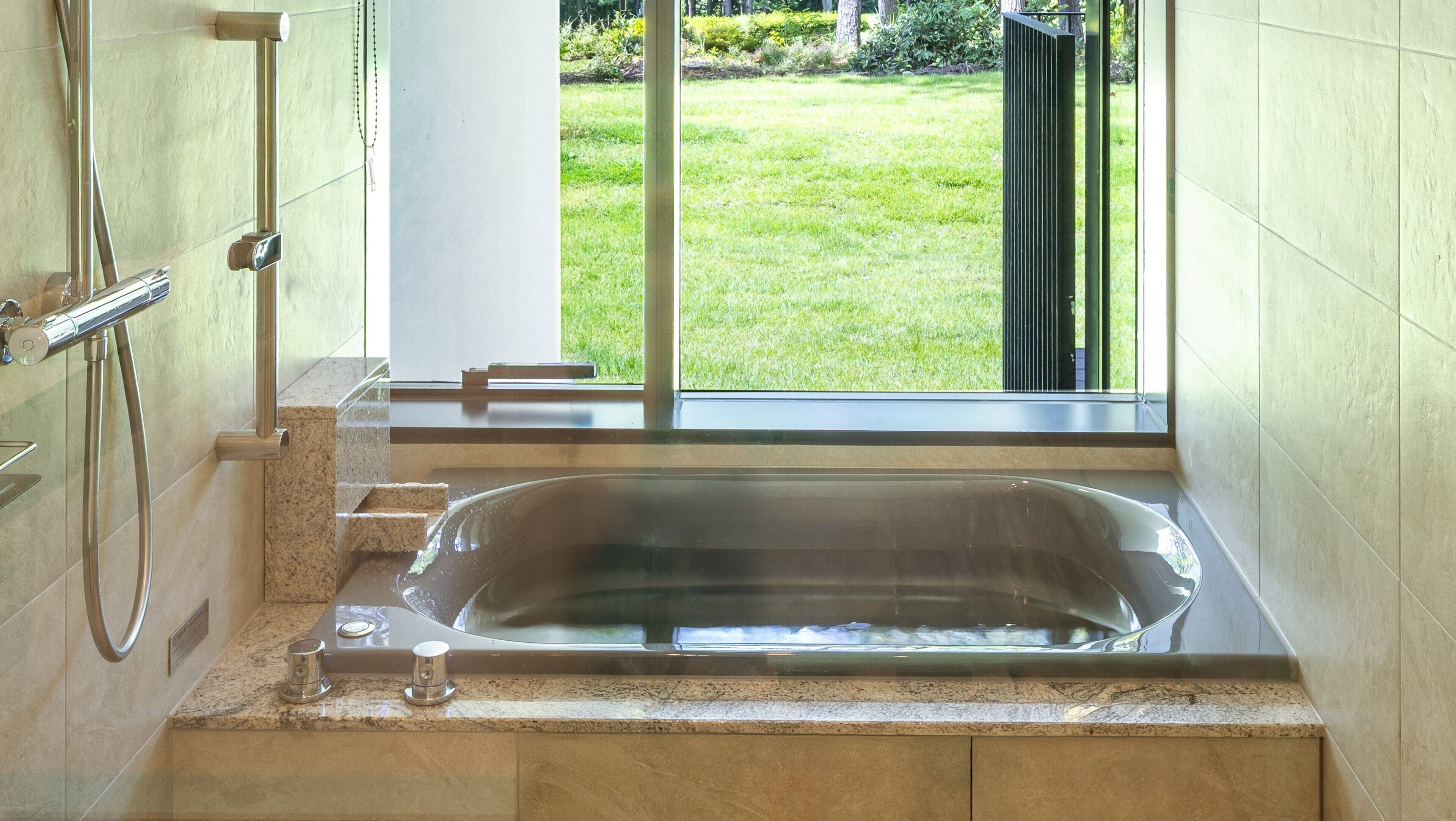 Un baño con una bañera grande, ducha y ventana con vista al jardín.