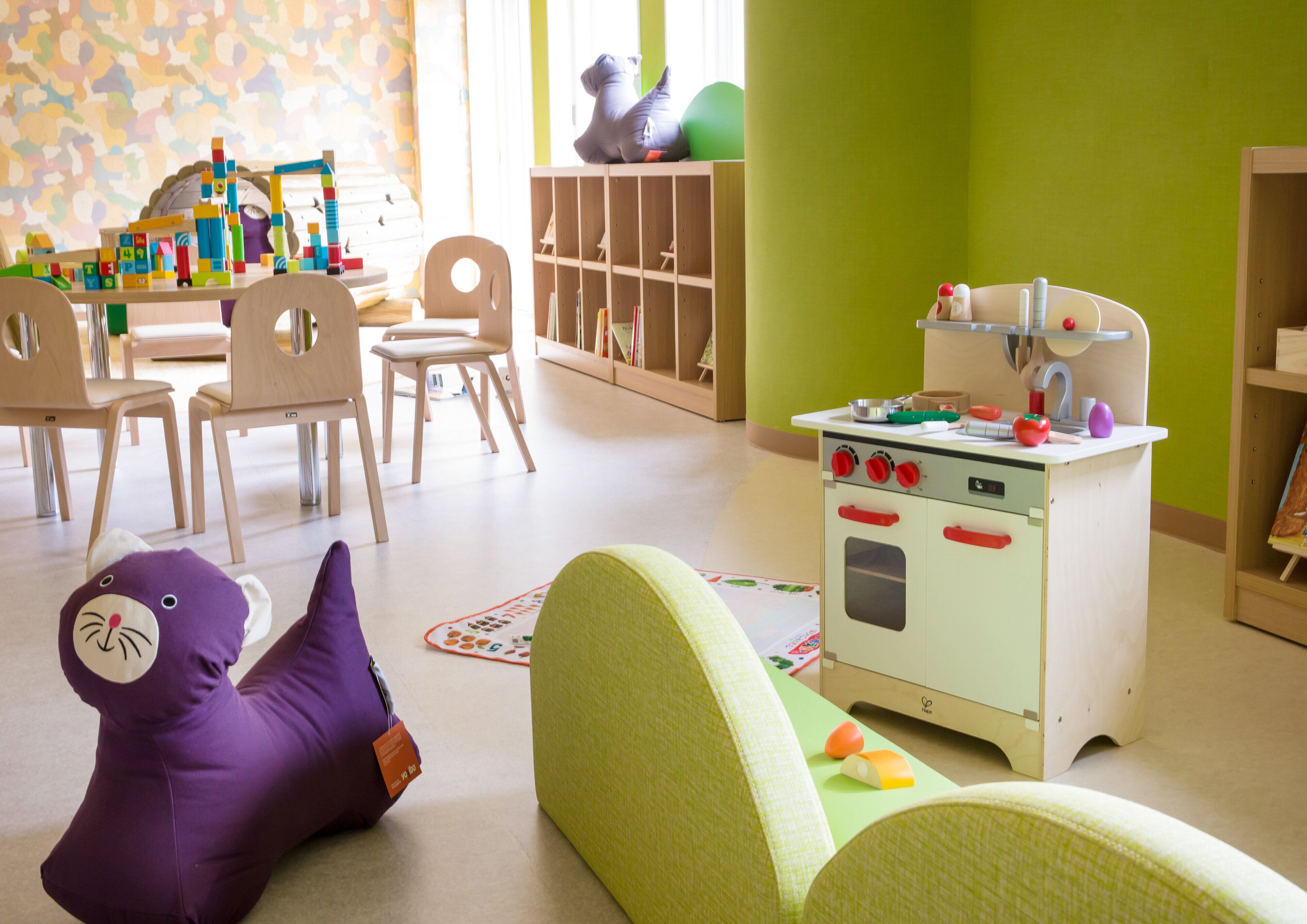 Uma sala de jogos infantil com cozinha de brinquedo, cadeiras e um elefante de brinquedo roxo.