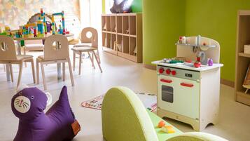 Uma sala de jogos infantil com cozinha de brinquedo, cadeiras e um elefante de brinquedo roxo.
