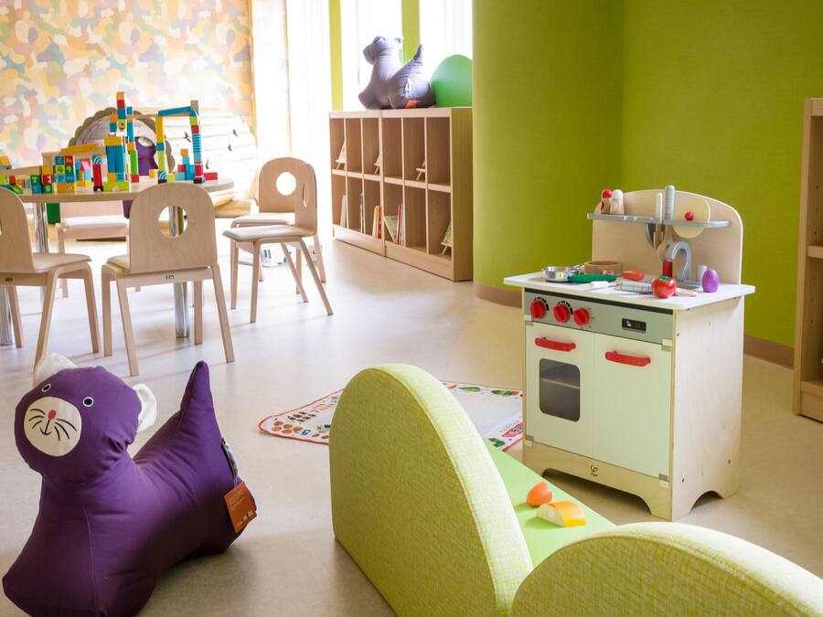 Uma sala de jogos infantil com cozinha de brinquedo, cadeiras e um elefante de brinquedo roxo.
