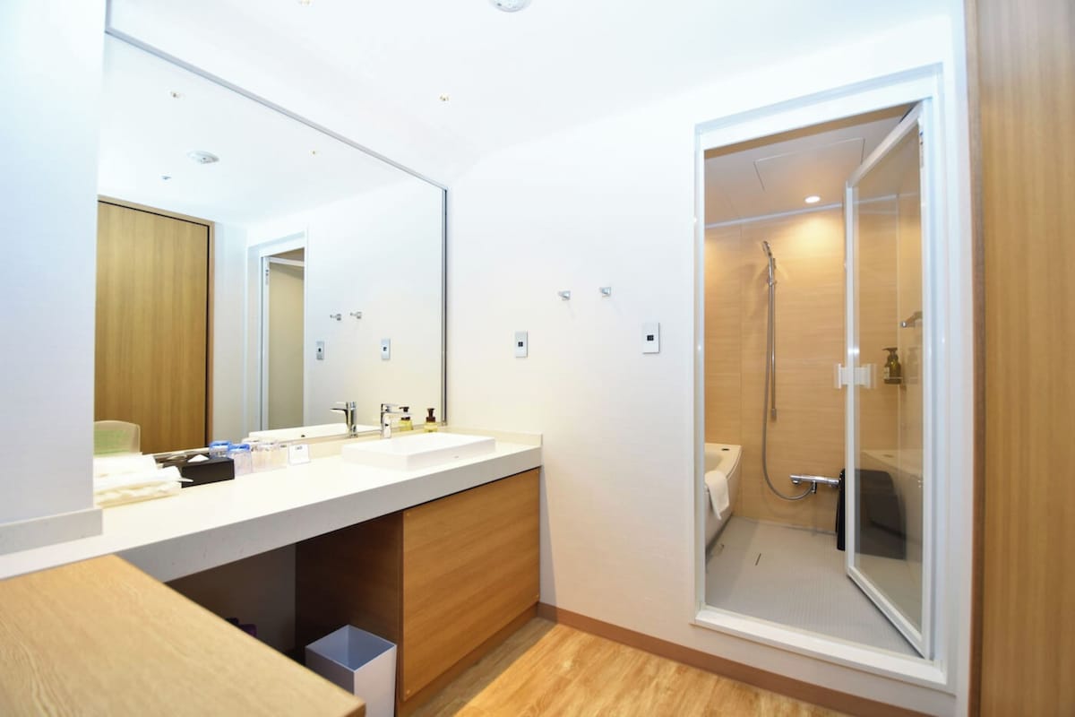 A modern bathroom with a large mirror, two sinks, and a glass-enclosed shower.